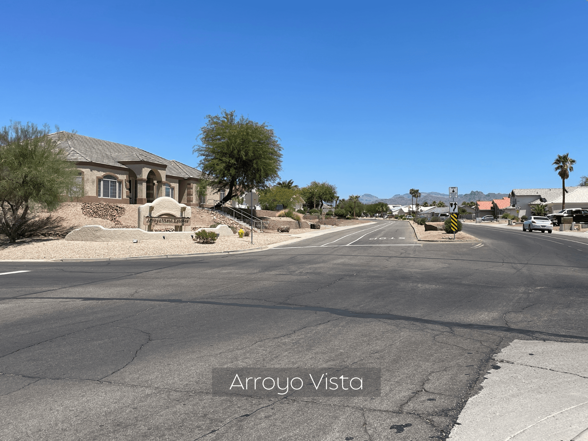 Sunny suburban street with desert landscaping under a clear blue sky.