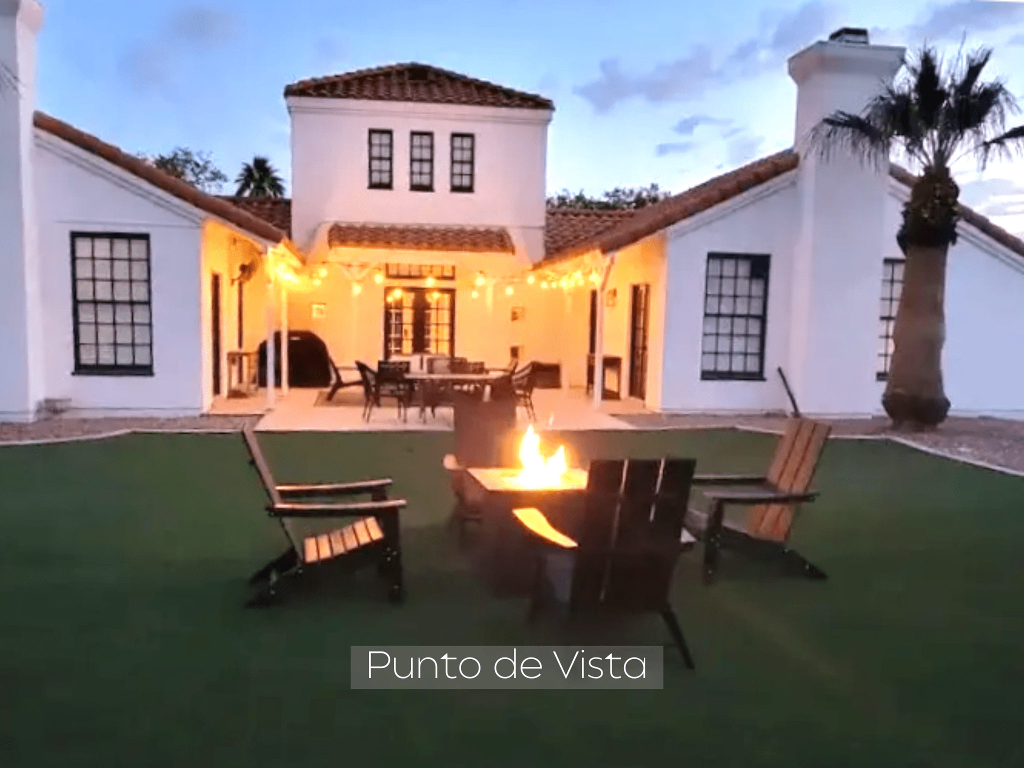 Cozy outdoor fire pit with chairs around a Spanish-style house at dusk.