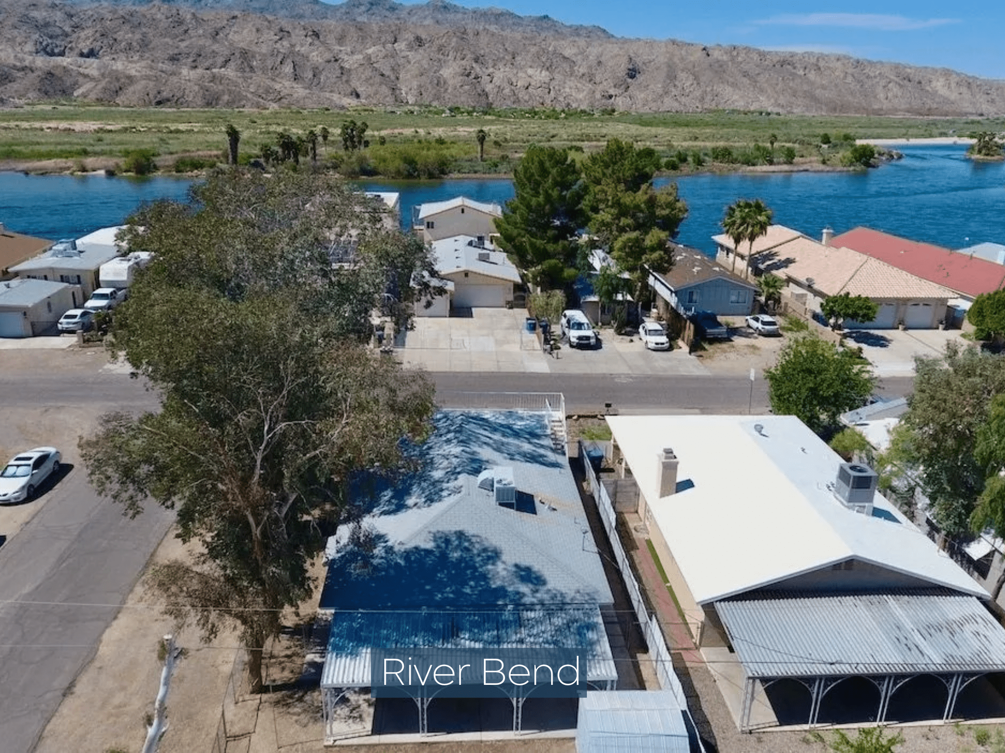 Aerial view of a river bend with houses and desert mountains in the background.
