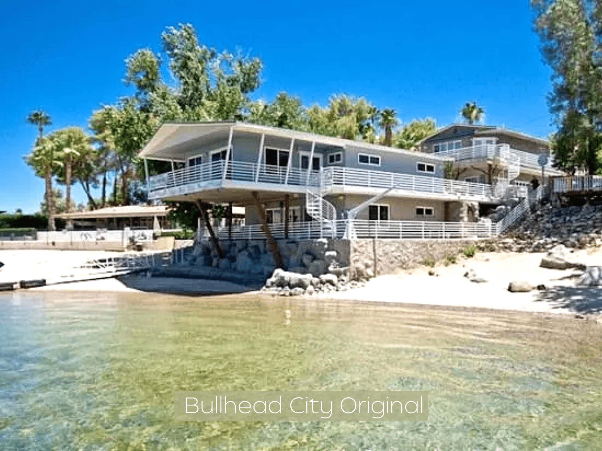 Modern house with large windows on a rocky beach under a clear blue sky.