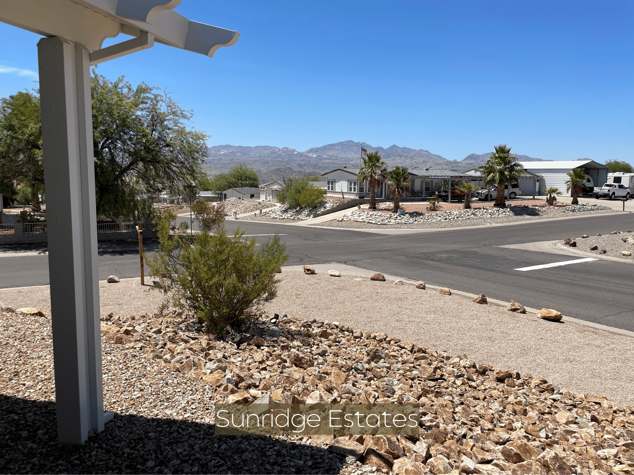 Desert neighborhood street with gravel landscaping and distant mountains.