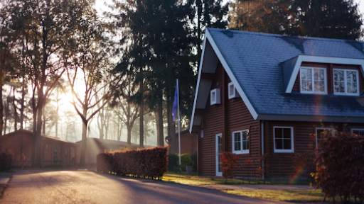 Cozy house with a snow-dusted roof in a serene, tree-lined neighborhood at sunrise.